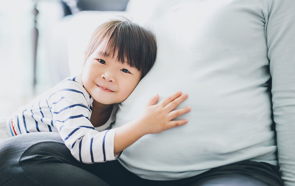 Asian daughter holding mother's pregnant belly.