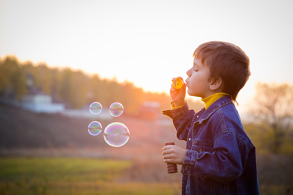 A young boy blows bubbles outside in a field.