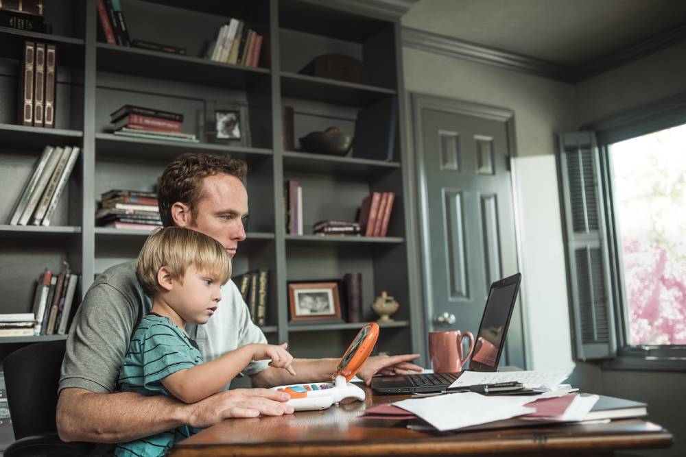 On-page, 2024. A father and his young son sitting in an at-home office and looking at computers.