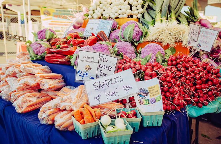 carrots, radishes and other vegetables sit on tables at a farmer's market